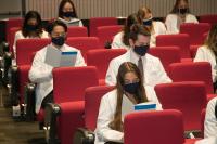 Students wearing white coats in staggered seating holding event booklets